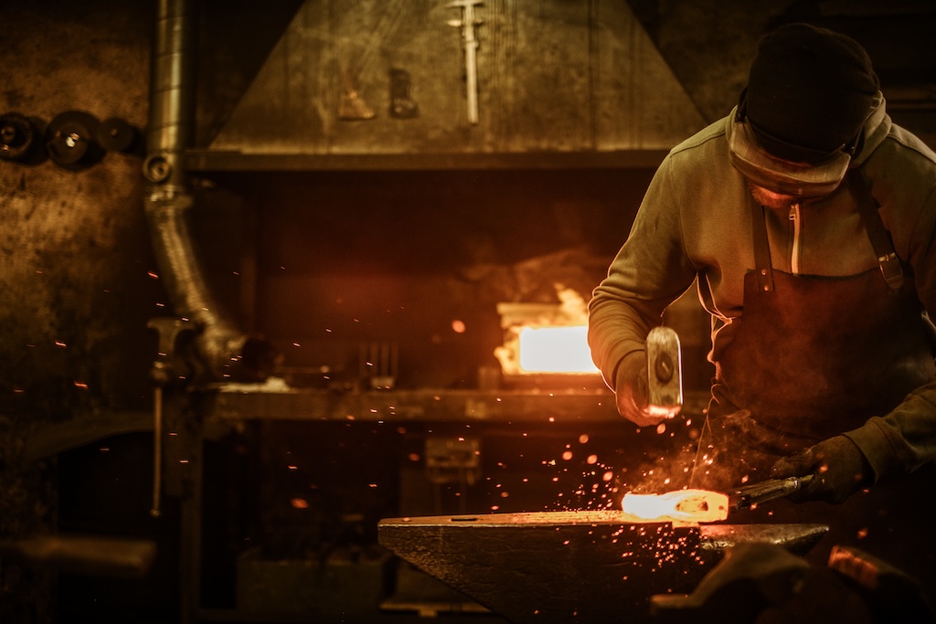 The blacksmith forging the molten metal on the anvil in smithy.